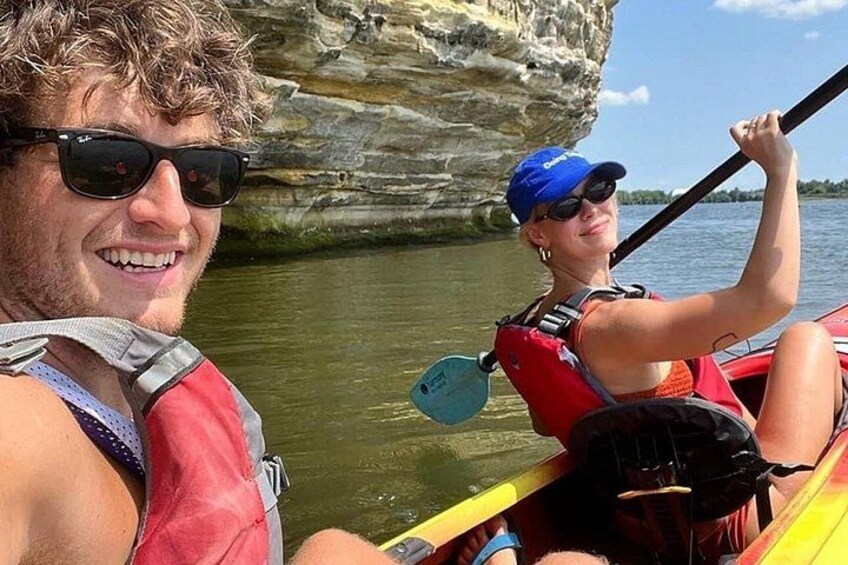 Two people in a canoe on a river with rocky cliffs in the background. 1