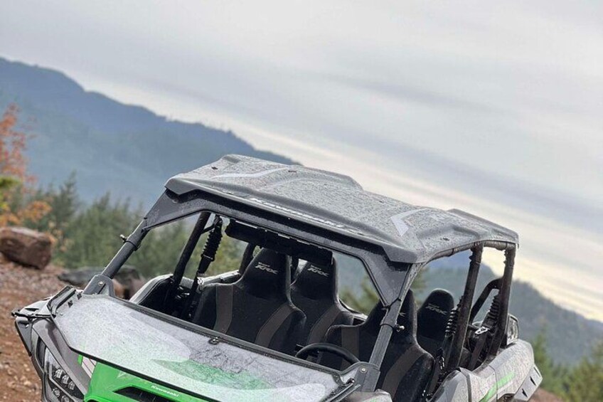 A green and black off-road vehicle parked on a rocky terrain with a mountainous landscape in the background. 1