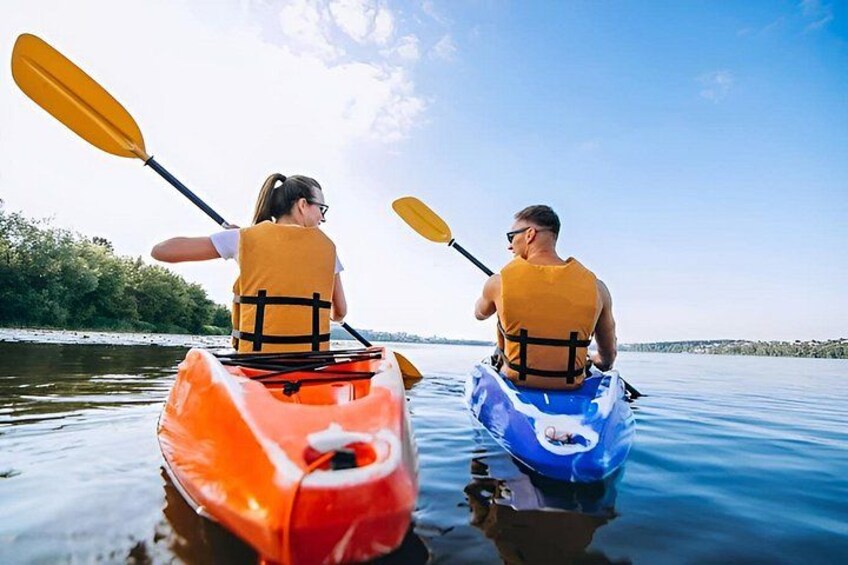Two people kayaking on a calm body of water with trees in the background. 3