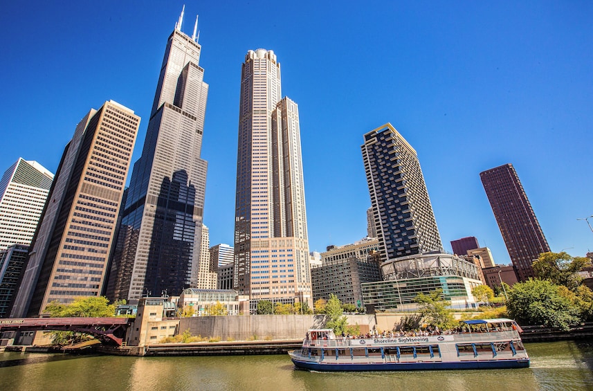 A city skyline with tall buildings and a river with a sightseeing boat. 2