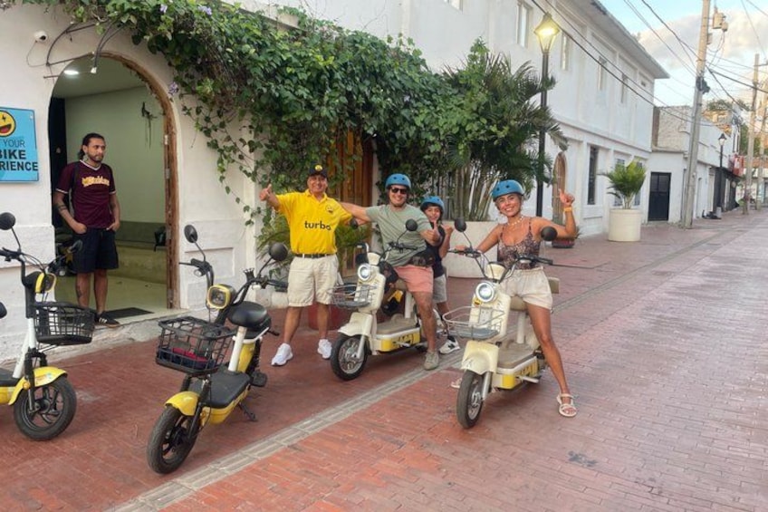 A group of people on scooters, a building with a sign, and a street. 2