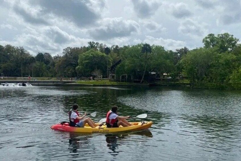 Two people kayaking on a calm lake surrounded by trees. 1