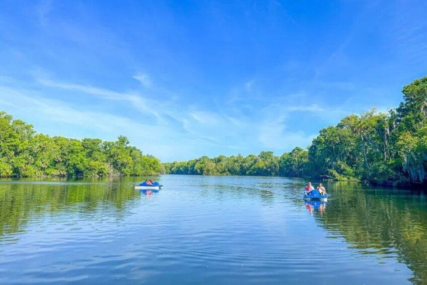 A calm river with two boats, one with people and another empty, surrounded by dense greenery. 1