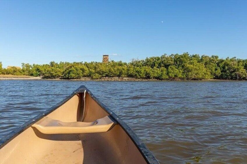 A canoe on calm water with a tree-lined shore in the background. 1