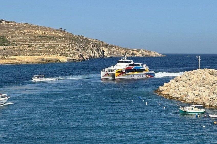 A colorful speedboat named 'GOZO' navigating near a rocky coastline with a smaller boat in the background. 2