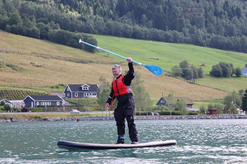 A person paddleboarding on a calm body of water with houses and greenery in the background. 3