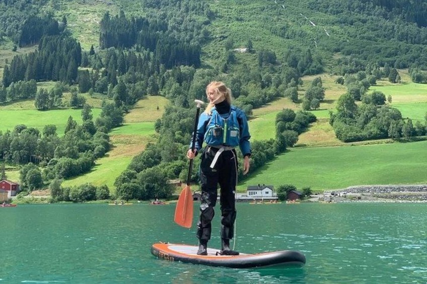A person standing on a paddleboard in a lake with a mountainous landscape in the background. 1