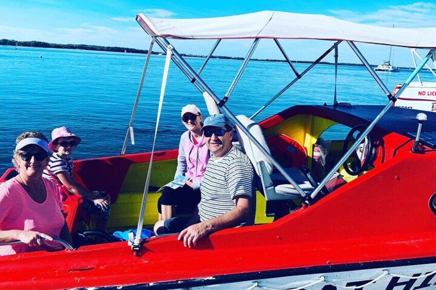 A red boat with a canopy, people on board, and calm water in the background. 1