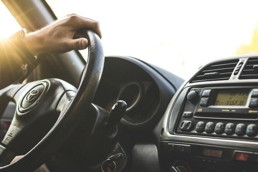 A hand on a steering wheel inside a car with a radio and a digital display. 4