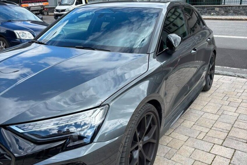 A dark-colored sedan parked on a paved surface. 1