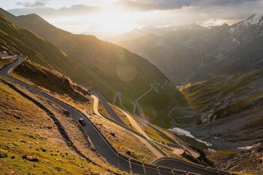 A winding mountain road with vehicles, surrounded by green hills and a valley. 3