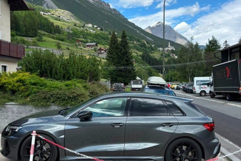 A grey car parked on a street with a mountainous landscape in the background. 5