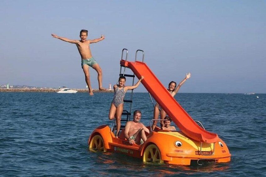 A person jumping off a slide into the water, a boat, and a clear sky. 3