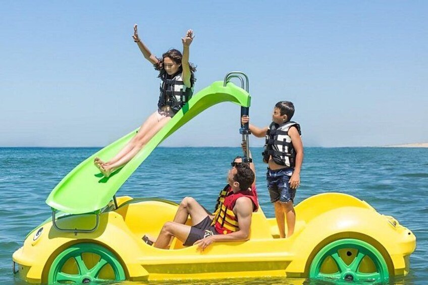 A yellow watercraft with a green slide, people on it, and a clear blue sky. 2