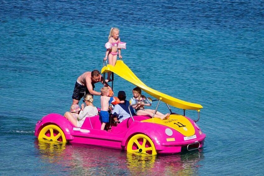 A pink inflatable boat with yellow wheels on water. 1