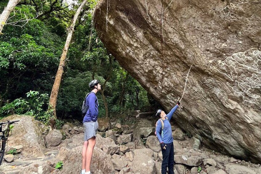 Two people climbing a large rock formation in a forested area. 2