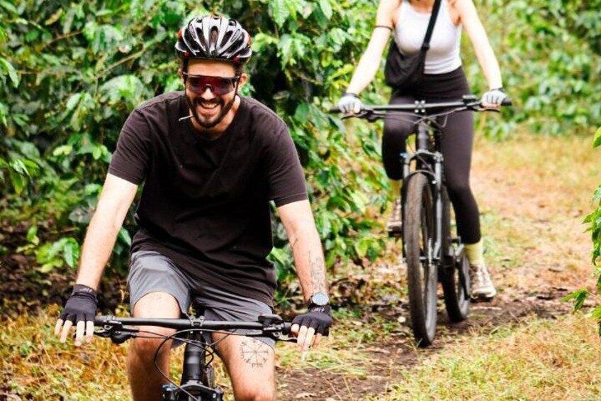 Two people riding bicycles on a dirt path surrounded by greenery. 1