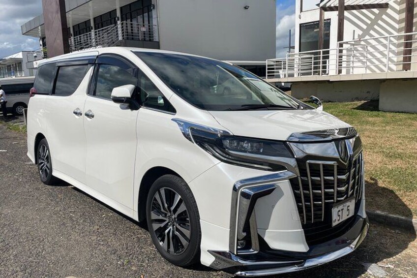 A white minivan parked on a gravel surface with a modern building in the background. 4
