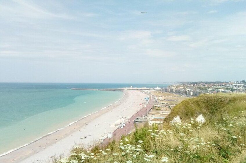 A coastal landscape with a beach, a promenade, and a distant cityscape. 3