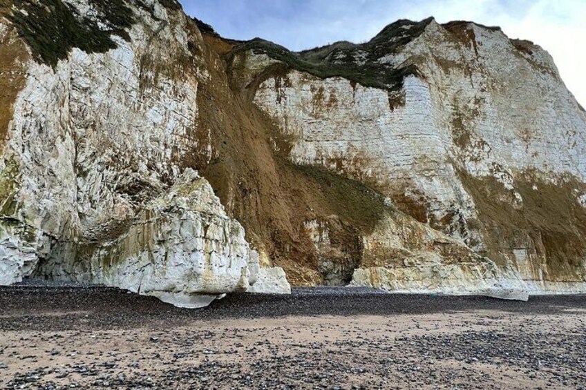 A coastal cliff with white and brown layers, a pebbly beach, and a clear sky. 2
