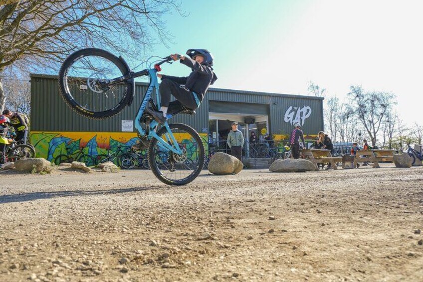 A person performing a bike stunt in a dirt area with a building in the background. 3