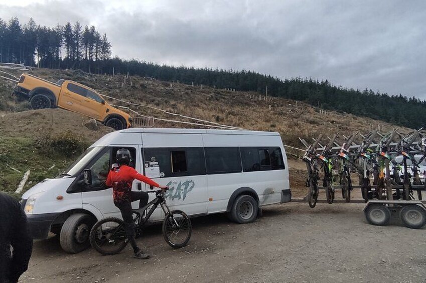 A white van parked on a dirt road with a person in a red shirt riding a bicycle. 1