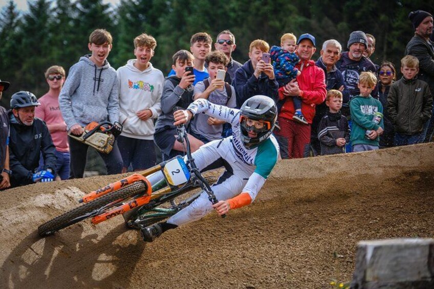 A motocross rider leaning into a turn on a dirt track with spectators in the background. 5