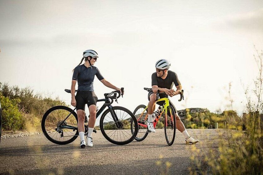 Two cyclists on a paved road with vegetation on the sides. 2
