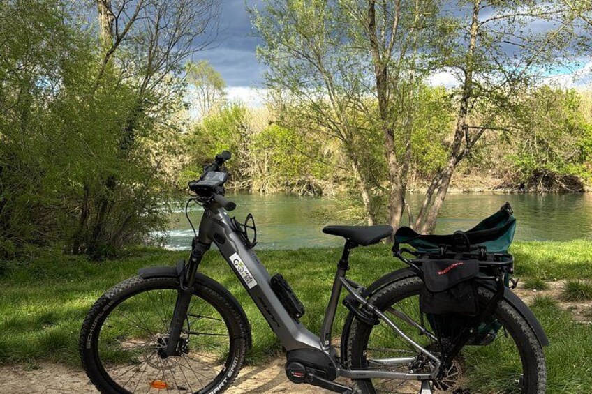 A mountain bike parked by a river with a green bag attached to the rear. 3
