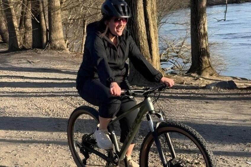 A person riding a bicycle on a gravel path near a body of water with trees in the background. 5