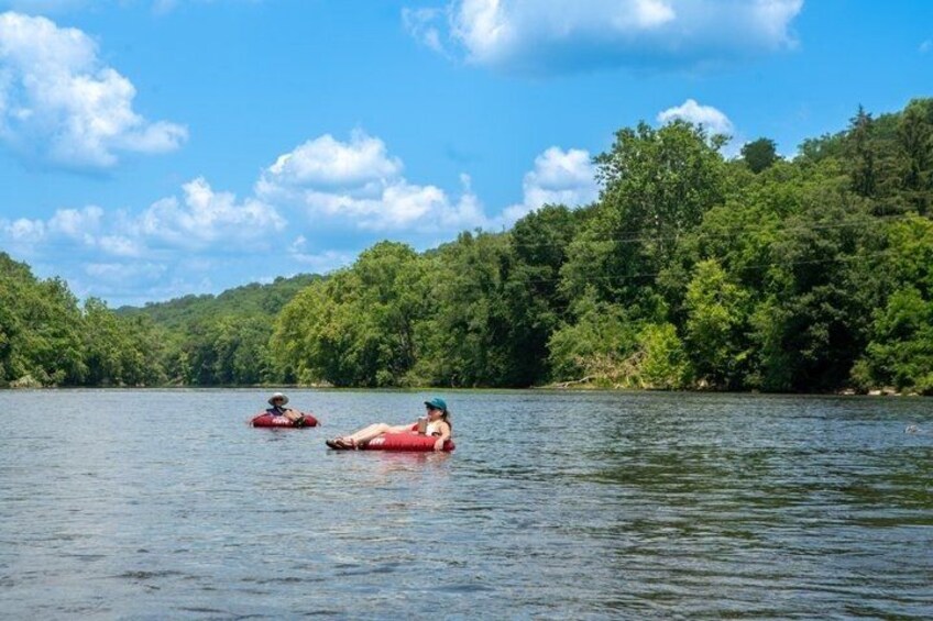 Two people floating on a calm lake surrounded by dense forest. 2