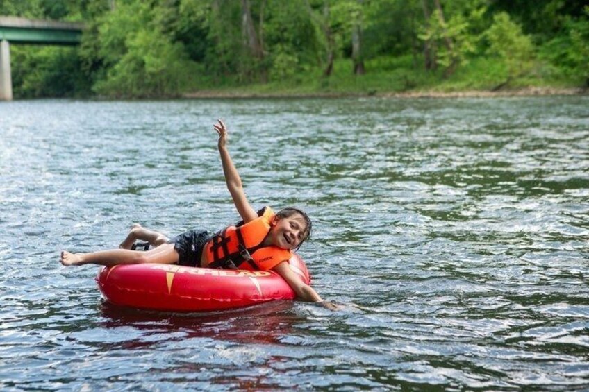 A person floating on a red tube in a body of water with trees and a bridge in the background. 3