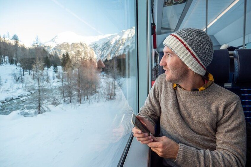 A person sitting by a window, holding a smartphone, with a snowy landscape and mountains in the background. 3