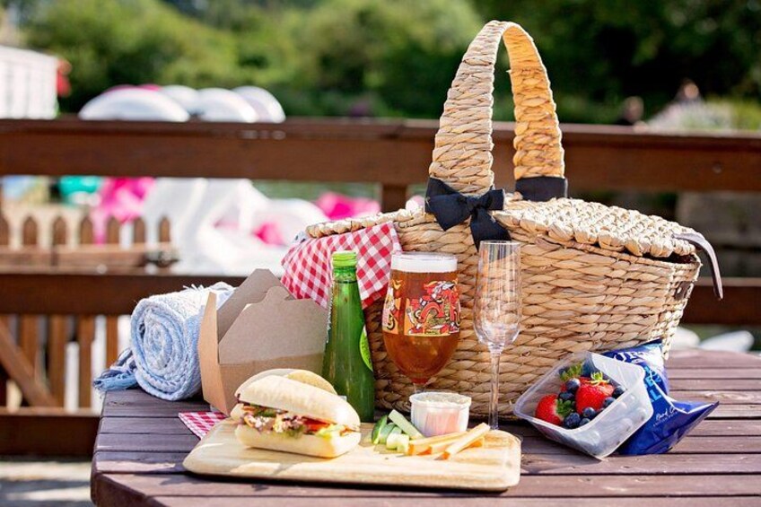 A picnic setup with a basket, sandwich, drink, and fruit on a wooden table. 5