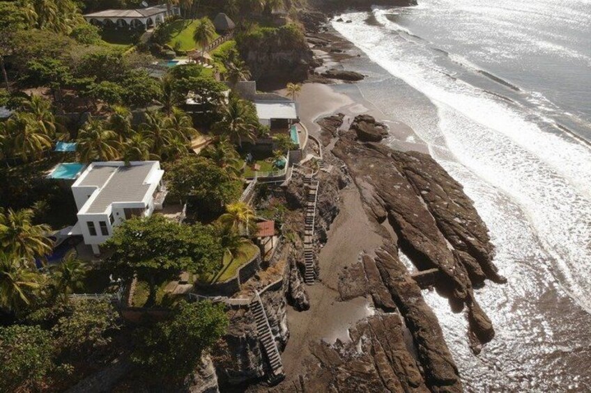 A coastal area with a rocky shoreline, a white building, and a staircase leading down to the beach. 3