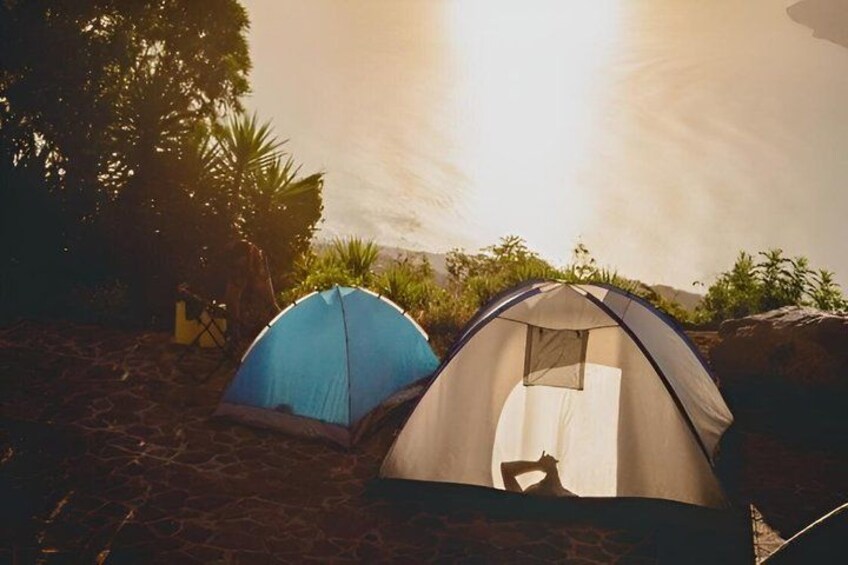 Two tents on a sandy beach with a body of water and vegetation in the background. 2