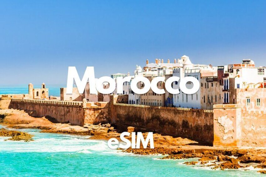 A coastal cityscape with historic buildings, a fortified wall, and clear turquoise waters. 1