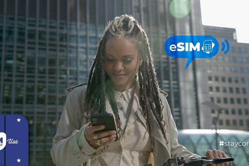 A person with braided hair holding a smartphone, standing in an urban environment with tall buildings in the background. 2