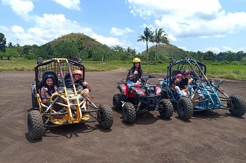 Three off-road vehicles on a dirt path with a hilly landscape in the background. 2