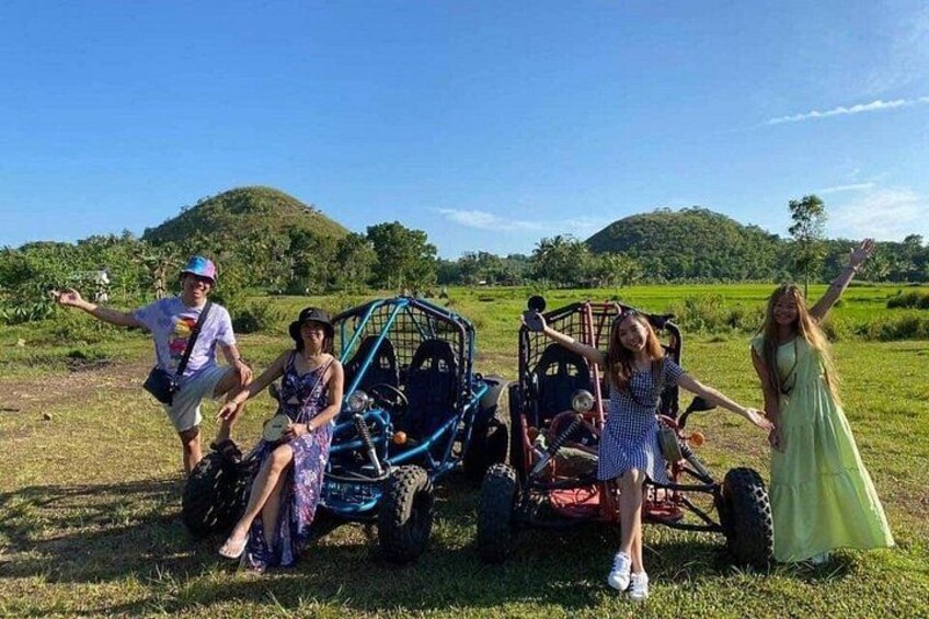 A group of people on a grassy field with a vehicle and a hill in the background. 1