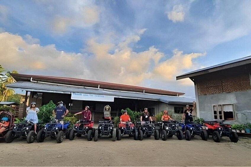 A group of people on ATVs lined up in front of a building with a sign. 3