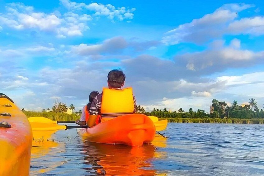 A person kayaking on a calm river with a clear sky and distant palm trees. 2