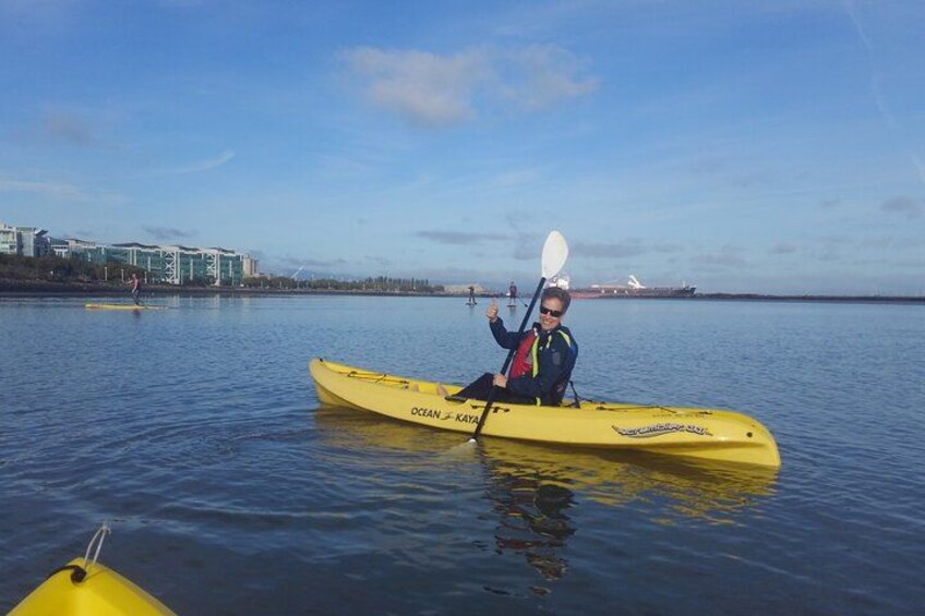 A person kayaking on calm water with a cityscape in the background. 1