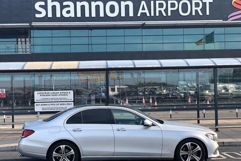 A silver car parked in front of a building with a sign that reads 'Shannon Airport.' 1