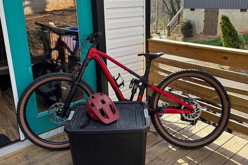 A red mountain bike on a wooden deck with a black trash bin and a red helmet. 3