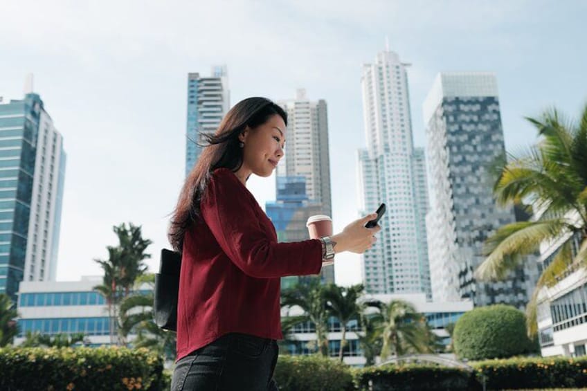 A person holding a smartphone and a coffee cup, with tall buildings in the background. 5