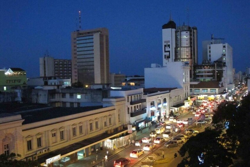 Una calle urbana al anochecer con edificios, vehículos y farolas. 5