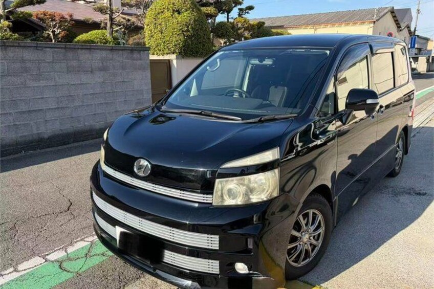 A black van parked on a street with a brick wall and a small tree in the background. 2