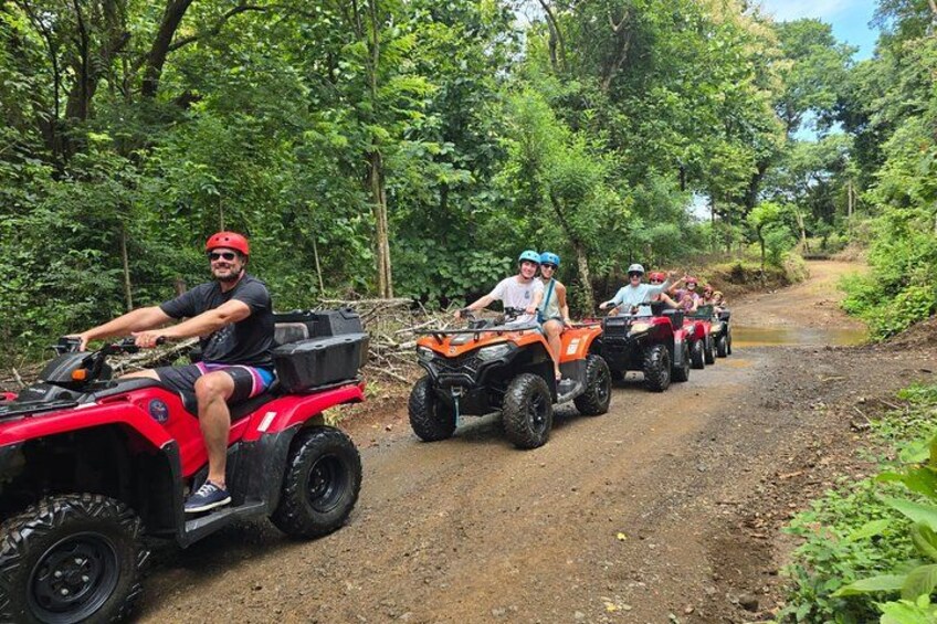 A group of people on ATVs on a dirt path surrounded by trees. 1