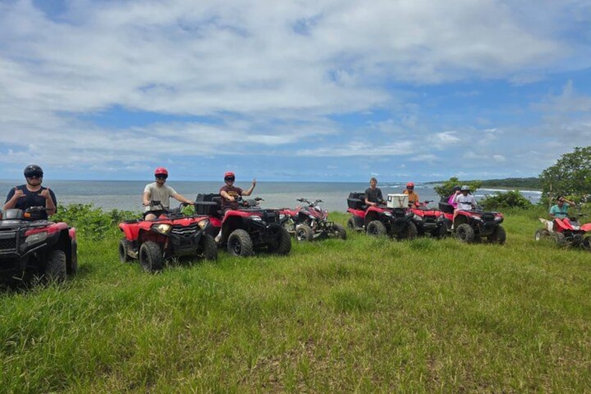 A group of people on ATVs in a grassy field with a body of water and a cloudy sky in the background. 2